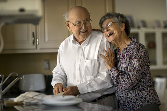 Smiling elderly couple share an affectionate moment while they do the dishes together.