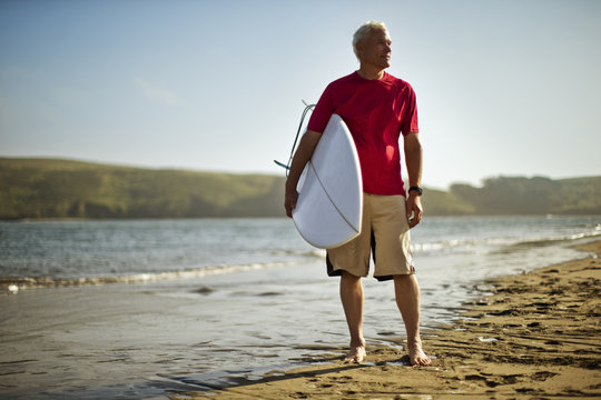 Portrait of a mature man carrying a surfboard on a beach.