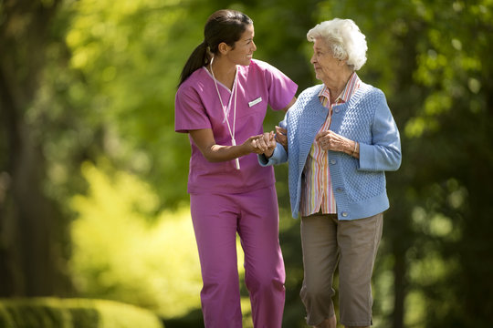 Happy young nurse helpfully assisting an elderly patient to walk outside.
