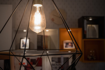 A glowing light bulb in modern lamp with blurred decoration shelf background