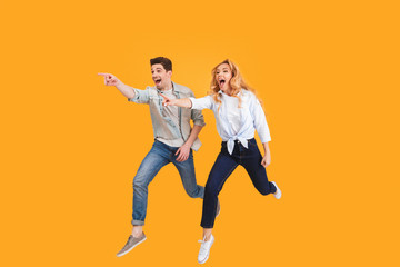 Full length image of happy caucasian man and woman shouting while pointing fingers aside at copyspace, isolated over yellow background