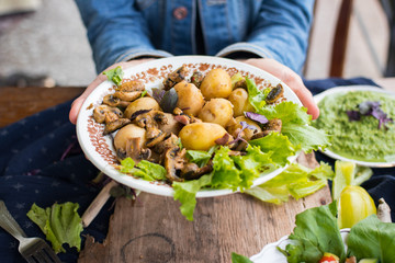 Woman hands holding backed potatoes and roasted mushrooms on salad leaves. Organic farm lunch or dinner. Raw vegan vegetarian healthy food