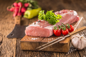Pork loin fillet parsley herb tomatoes pepper garlic salt and spices on wooden kitchen board.
