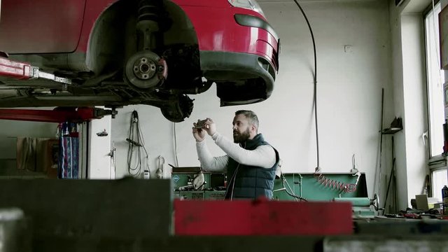 Man mechanic with smartphone repairing a car in a garage.