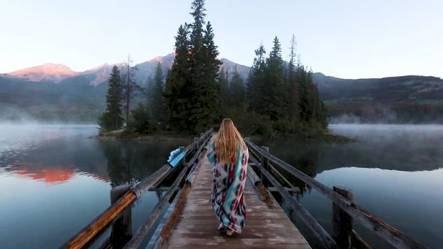 A woman walking over a bridge towards a foggy island in the middle of a Canadian lake