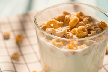 side view cup of milk with cereal rings in a sunny morning as healthy breakfast close up