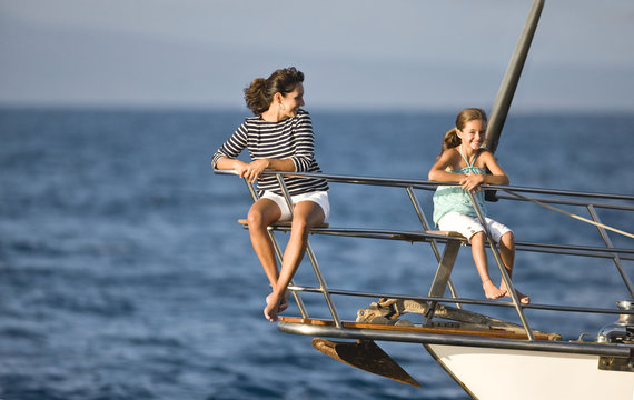 Little girl and woman sitting on yacht railing.