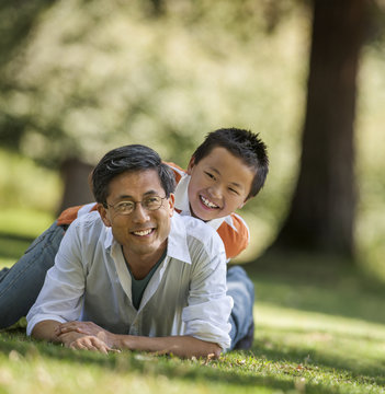 Portrait of a smiling father and his young son lying in the park.
