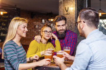 Group of four people toasting with glasses full of beer in local pub