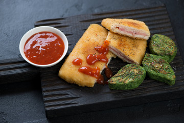 Close-up of chicken cordon bleu with vegetable nuggets and sauce on a black wooden serving board