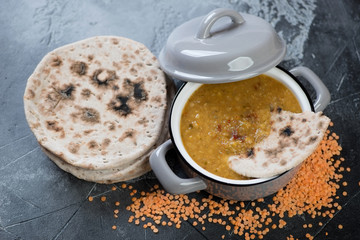 Pan with thick indian red lentil soup and chapati flatbread, horizontal shot on a grey concrete background, selective focus