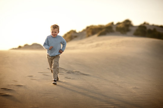 Boy running along a beach at sunset.