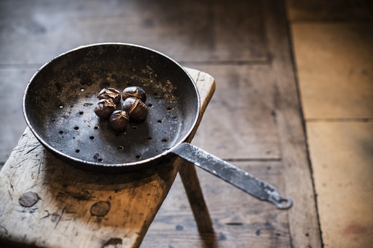 High angle close up of frying pan with freshly roasted chestnuts on rustic wooden table.
