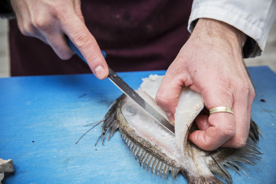 High angle close up of fishmonger filleting John Dory fish with knife on blue chopping board.