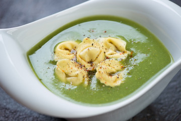 Closeup of broccoli cream-soup with tortellini served in a white bowl, selective focus