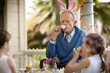 A grandfather having a tea part with his granddaughters.