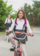 Obraz premium Portrait of beautiful girl in school uniform and bag riding to school on bicycle
