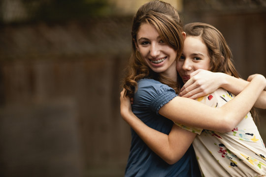Teenage girl smiles as she stands with her arms around her friend.