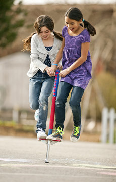 Two friends happily playing on a pogostick.