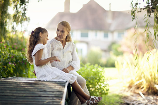 Young girl sits on a footbridge talking to her grandmother.