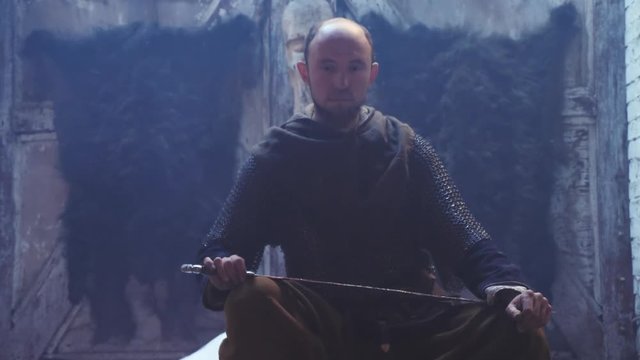 Portrait of a Viking warrior with sword in the hands sitting by the fire.