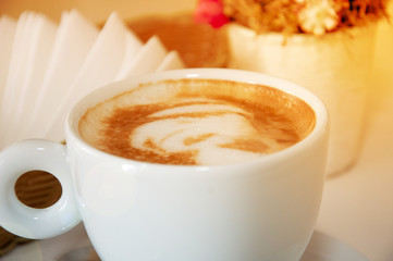 Coffee cappuccino in a white cup close-up. In the background, flowers and napkins, background with space for text.