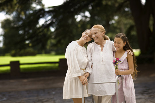 Grandmother, daughter, and granddaughter stand together outdoors at a park.