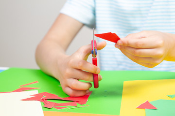 Child hands cutting colored paper with scissors at the table