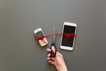 Old phone and new smartphone connected by red pulse laying on grey paper background. Scissors cut...