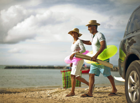 Couple walking to the beach with swim rings and beach mats.