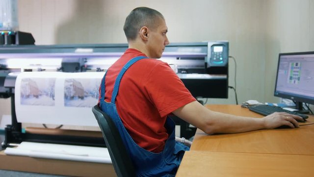 Male worker in typography with computer in front of printing press