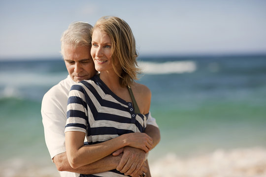Mature man hugging his wife on the beach.