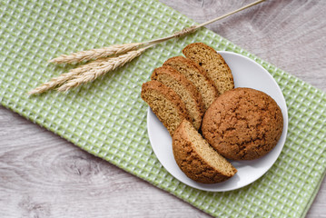 Homemade cookies on a white saucer and green napkins, spikelets of wheat on a wooden background