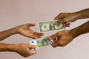 Close up on hands of man and woman exchanging currency notes, five euro and one US dollar bills on white background.