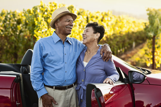 Happy senior couple standing next to their convertible by the vineyard.