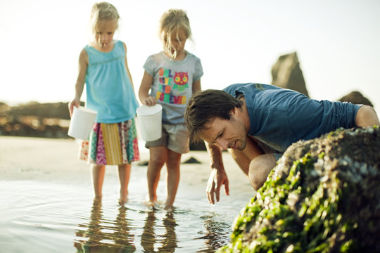 Mid-adult man looking at rock pool with his two young daughters.