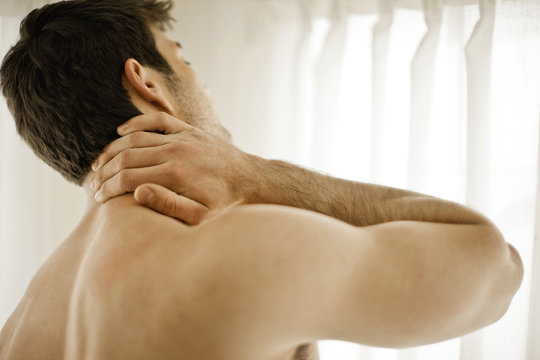 Shirtless young man rubbing his neck in pain.