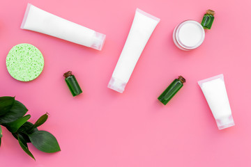 Cosmetics for skin care with natural ingredients. Eco cosmetics. Cream, lotion, oil, tonic near young green leaves on pink background top view copy space