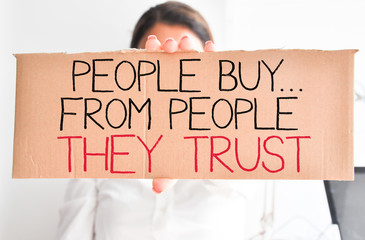 Business woman holding white card with text “people buy from people they trust”
