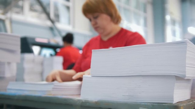 Paper stack in front of female worker sorting a papers in the typography