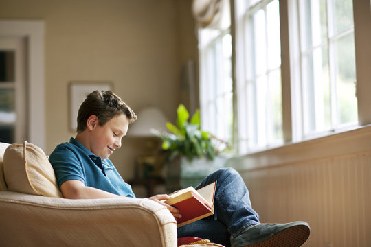Teenage boy sitting in a living room reading a book.