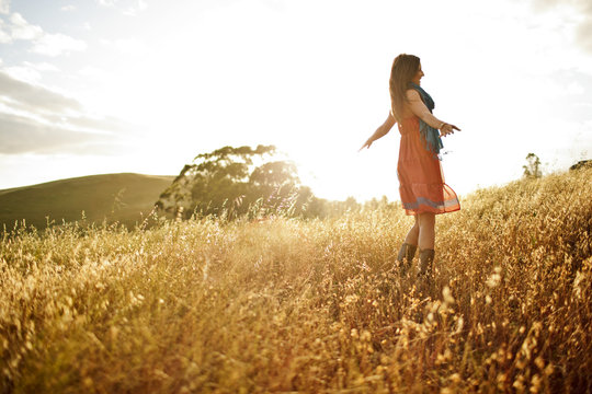 Young woman standing with her arms outstretched in a grassy field.