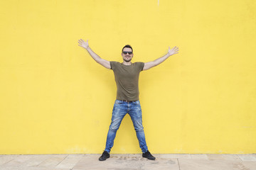 Man wearing sunglasses and posing against a yellow wall