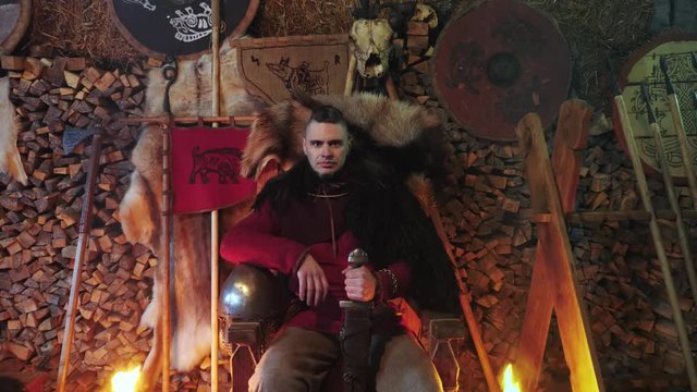 Portrait of a Viking warrior seated on a throne with a sword in his hands.