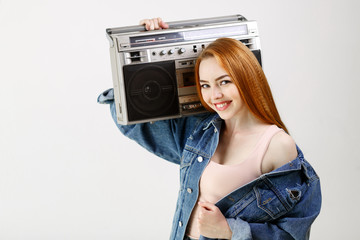 beautiful red-haired woman in a denim jacket holding retro tape recorder on a white background