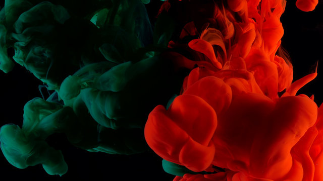Red and green ink in water shooting with high speed camera. Bloody paint dropped, reacting, creating abstract cloud formations and metamorphosis on black. Art backgrounds.