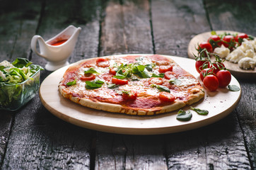 Italian food, cuisine. Margherita pizza on a black, wooden table with igredients like tomatoes, salad, cheese, mozzarella, basil. Delicious homemade food. 