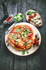 Italian food, cuisine. Margherita pizza on a black, wooden table with igredients like tomatoes, salad, cheese, mozzarella, basil. Delicious homemade food. 
