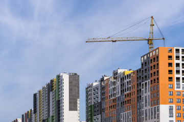 Fototapeta na wymiar large yellow construction crane, multi-storey house against the blue sky