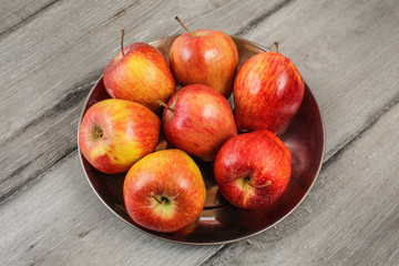 Metal bowl full of red ripe apples placed on gray wooden desk.
